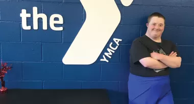 integrated fitness participant, colin, smiling next to a YMCA sign