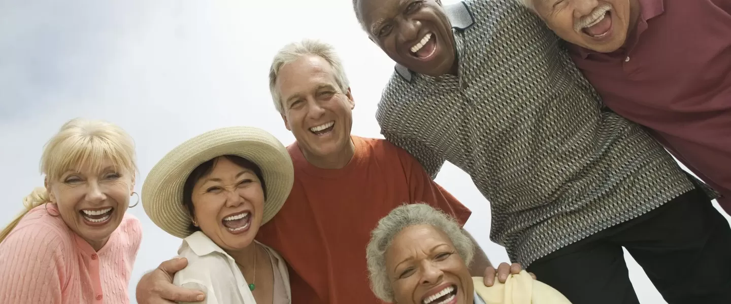 An image of a diverse group of older men and women pictured arm-in-arm, smiling for the photo.