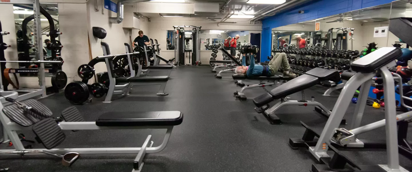 Free weight area with dumbbells, benches facing mirrors, and weight machines.