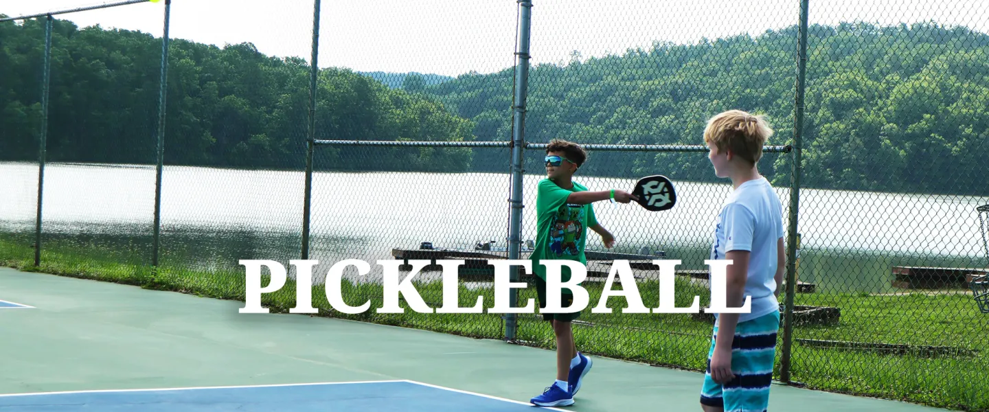 Campers holding paddles and playing an active game of pickleball on the outdoor courts.