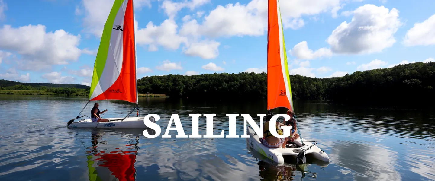 Campers navigating a small sailboat across Lake Sunnen on a sunny day.