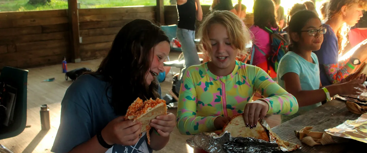 Quesadillas being cooked in foil packets over an open campfire during outdoor living skills.