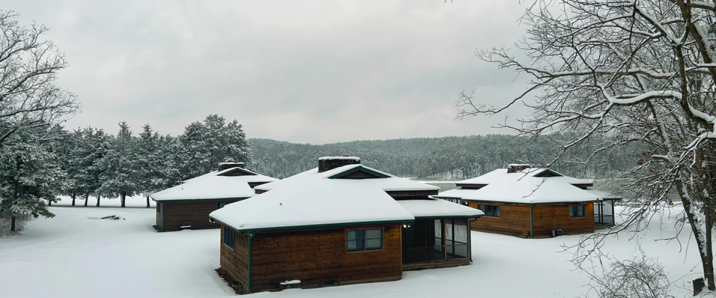YMCA Trout Lodge Lake View Family Cabins covered in white winter snow next to the Ozark Hills evergreen trees covered in snow and a frozen Sunnen Lake
