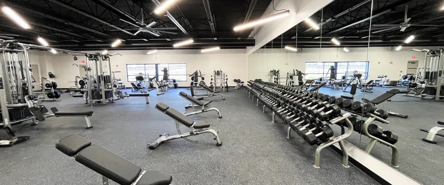 Renovated weight room at East Belleville YMCA featuring rows of dumbbells, adjustable benches, and large mirrors for strength training.