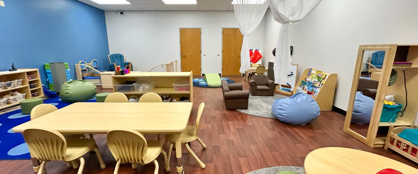 A cozy corner of the Ste. Genevieve YMCA Child Watch room showing a book display, bean bag chairs, and a wall-mounted mirror next to a play area for toddlers.