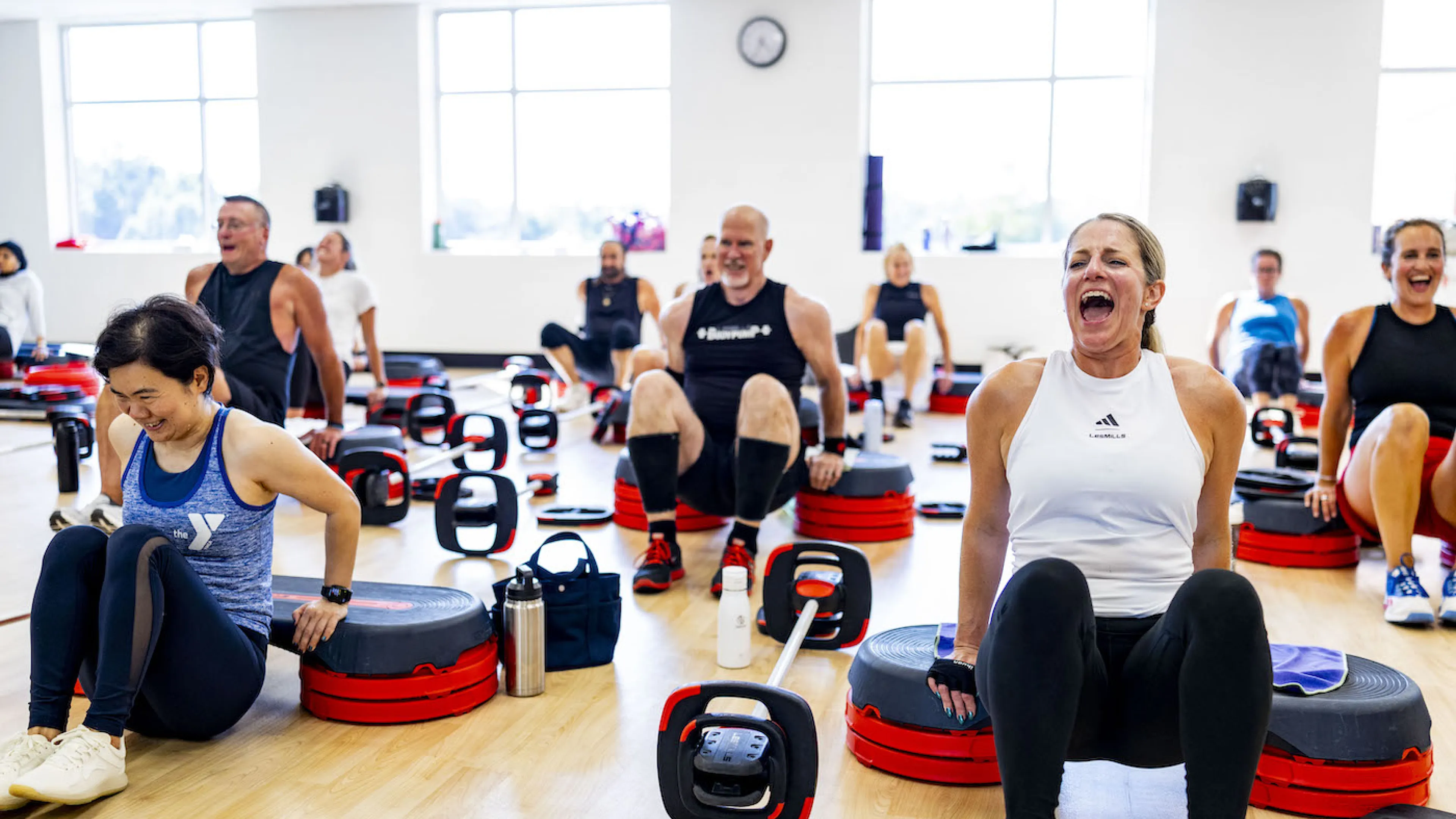Les Mills Bodypump YMCA Group Exercise Class participants smile next to BODYPUMP steps holding the class weight bars