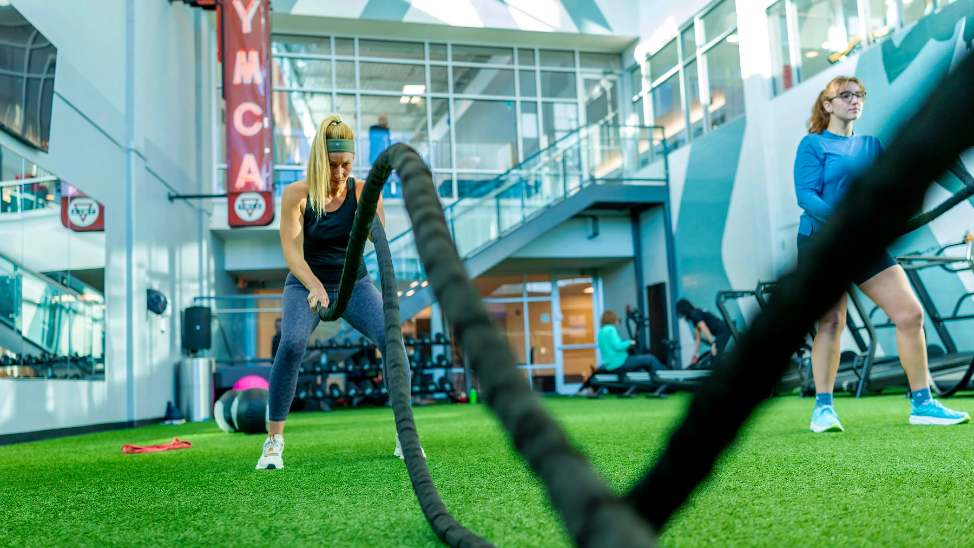A woman has a focused and determined look on her face as she uses workout battle ropes during a small group training Functional Fitness group exercise class at a St. Louis Missouri YMCA.